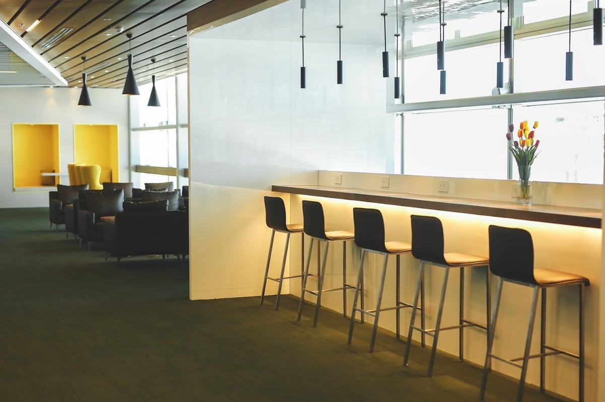Modern seating at CIP Orchid Lounge 1, Da Nang Airport Terminal 2, featuring high stools at a counter with power outlets, tulip flower arrangement, pendant lighting, and lounge chairs in the background.