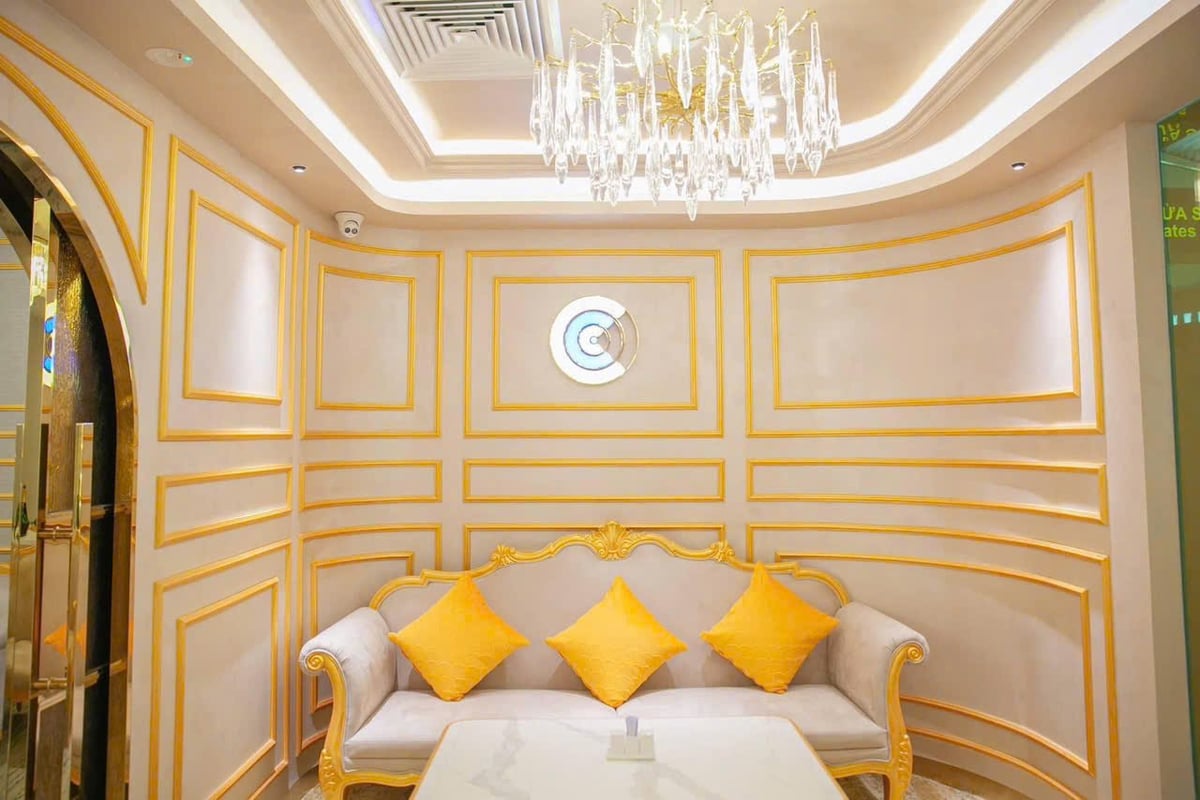 Elegant seating area inside Nam A Bank Premier Lounge at Da Nang Airport, featuring a gold-trimmed sofa with yellow cushions, decorative wall molding, and a crystal chandelier under ambient lighting.