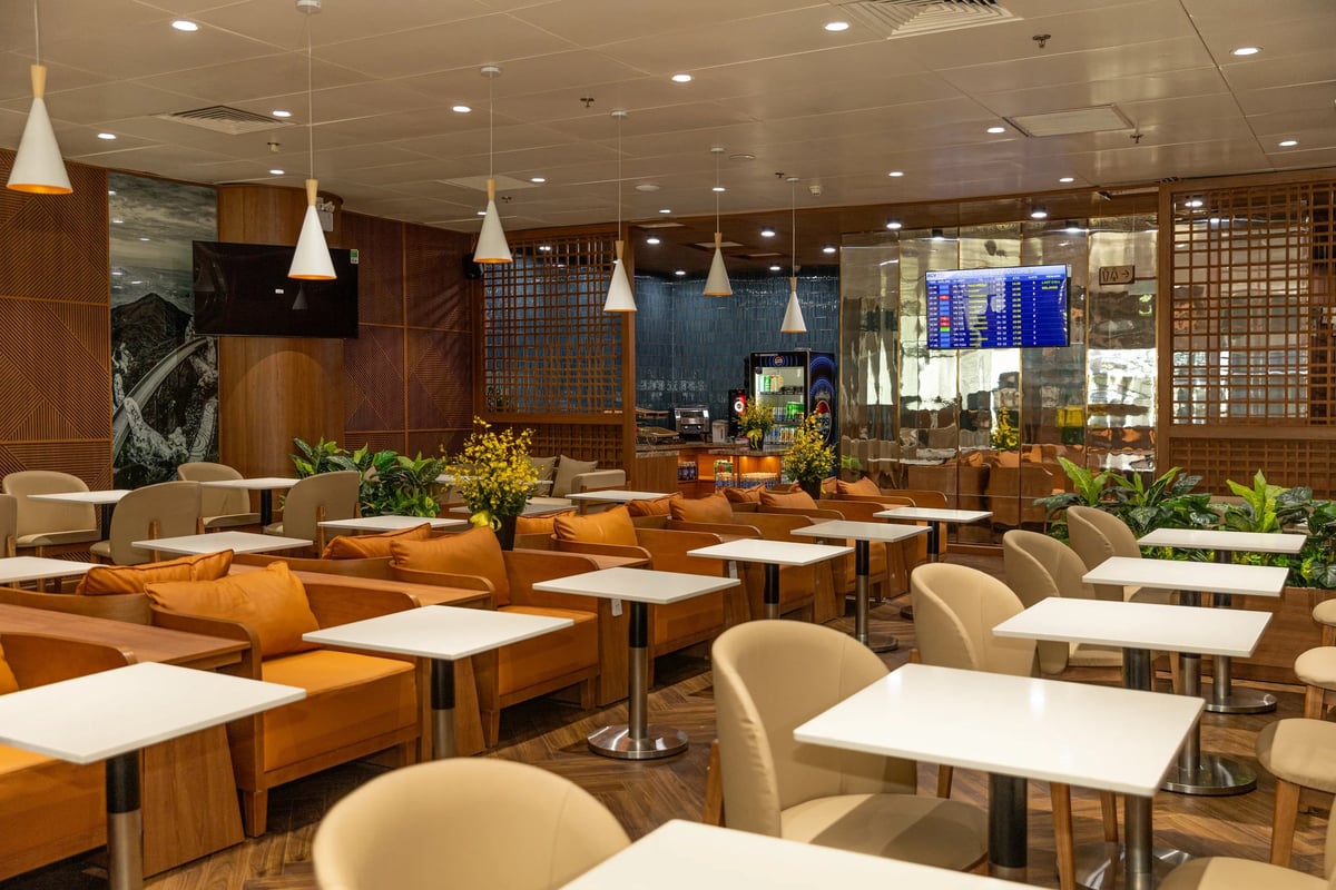 SH Premium Lounge at Da Nang International Airport – modern seating area with orange armchairs, white tables, pendant lighting, digital flight board, and refreshment station in a warm wood-accented interior.