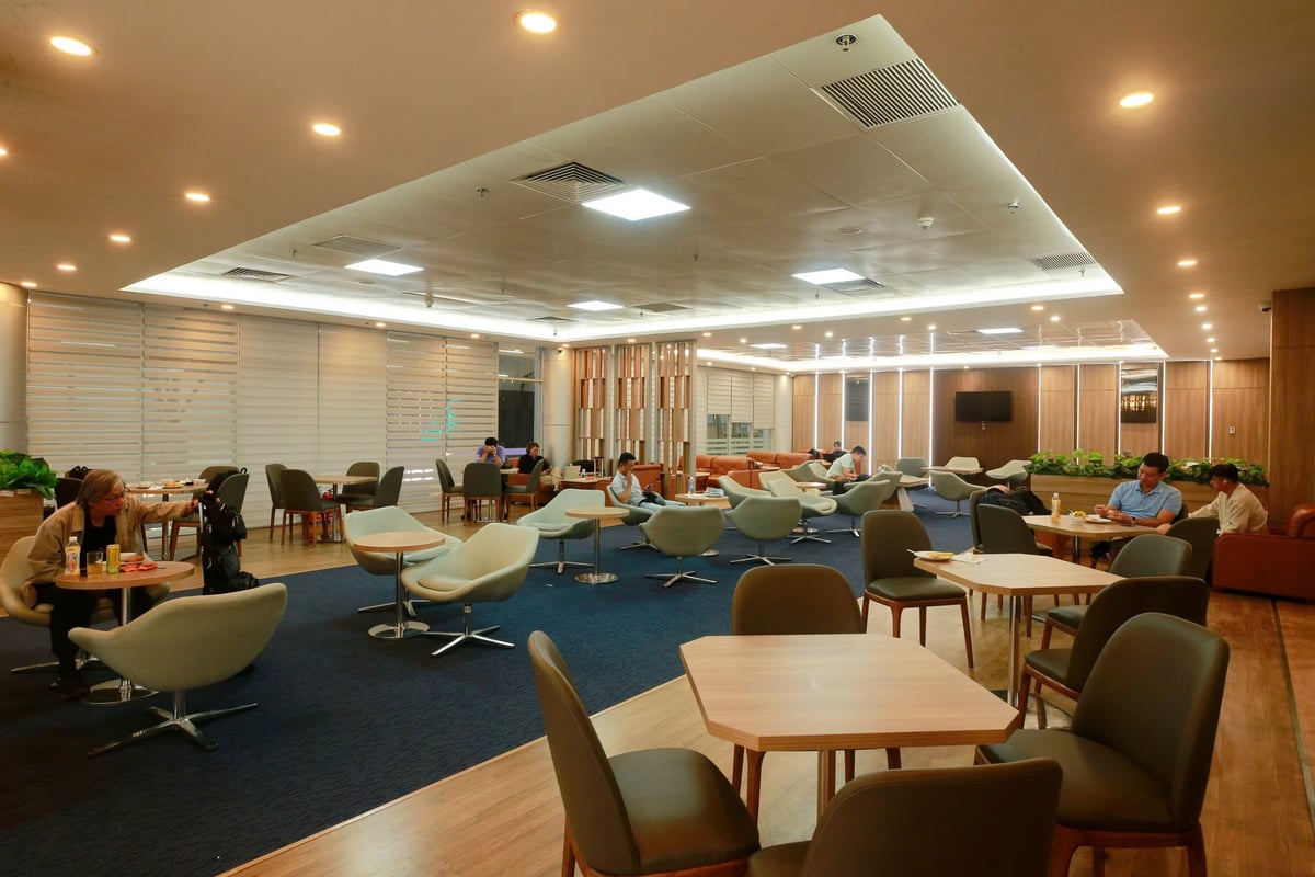 Spacious seating area at Vietnam Airlines Lotus Lounge in Da Nang Airport, featuring a mix of modern armchairs and dining tables, soft lighting, wood paneling, and relaxed travelers enjoying meals and quiet time.