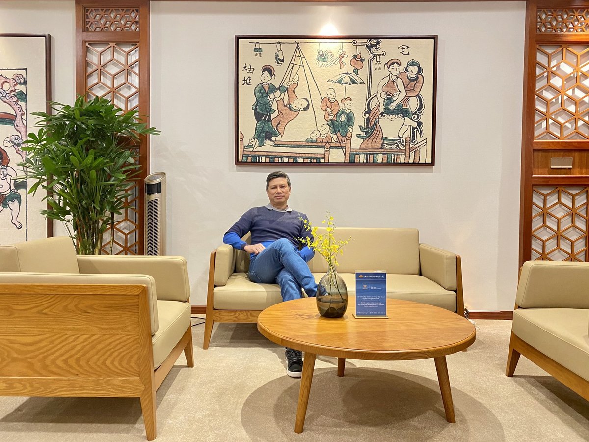 Guest relaxing in the Vietnam Airlines Lotus Lounge at Da Nang International Airport, surrounded by modern wooden furnishings, traditional Vietnamese artwork, and soft beige seating.