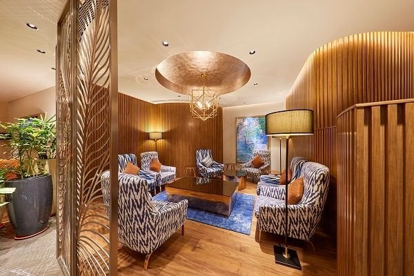 This image shows a luxurious lounge area, featuring a richly textured interior with a combination of wood paneling and modern furnishings. The seating area includes four armchairs upholstered in a blue and white ikat pattern.