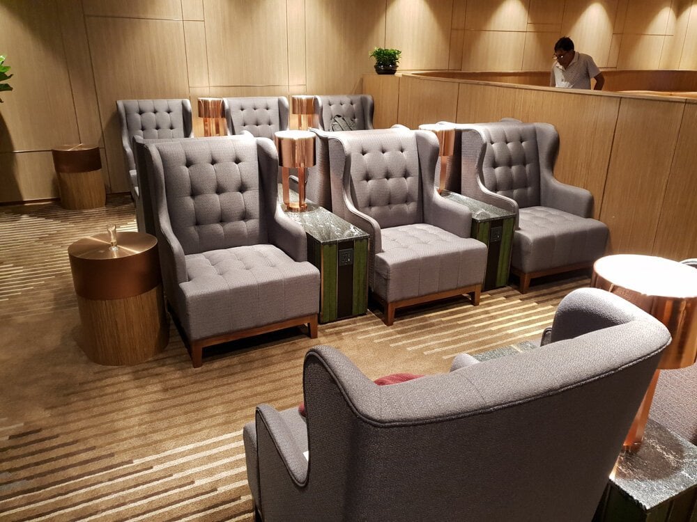 Plush armchair seating at Plaza Premium First Lounge, Hong Kong Airport – featuring high-backed, tufted chairs, individual side tables with built-in power outlets, and a cozy, wood-paneled ambiance ideal for relaxation.