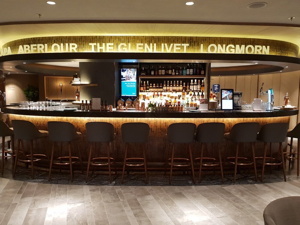 Elegant whisky bar at Plaza Premium First Lounge, Hong Kong International Airport – featuring top-shelf spirits including The Glenlivet, Aberlour, and Longmorn, with stylish seating and ambient lighting.