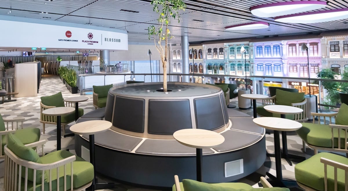 Seating area at Blossom Lounge Changi Airport Terminal 4 with greenery, modern furniture, and Peranakan-style shophouse view.