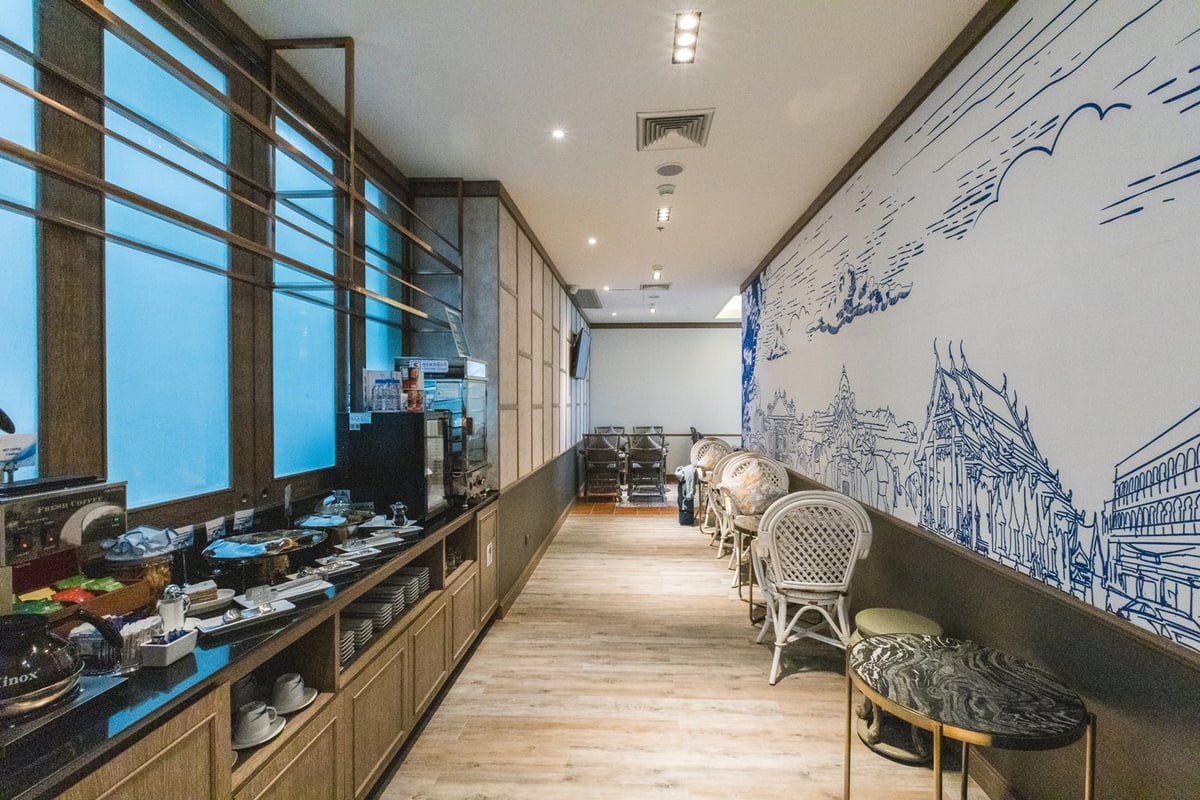 This image shows the interior of the Blue Ribbon Lounge at Phuket Airport, featuring a stylish and narrow buffet area. The room is lined with large windows on one side, filling the space with natural light.