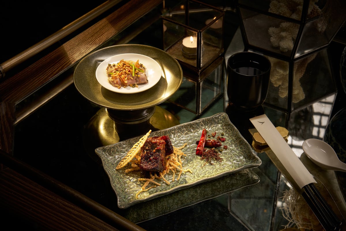 A refined dinner setting at The Pier First Class Lounge in Hong Kong International Airport, featuring braised wagyu beef with aged tangerine peel served on a textured ceramic plate with crispy noodles and dried chilies.