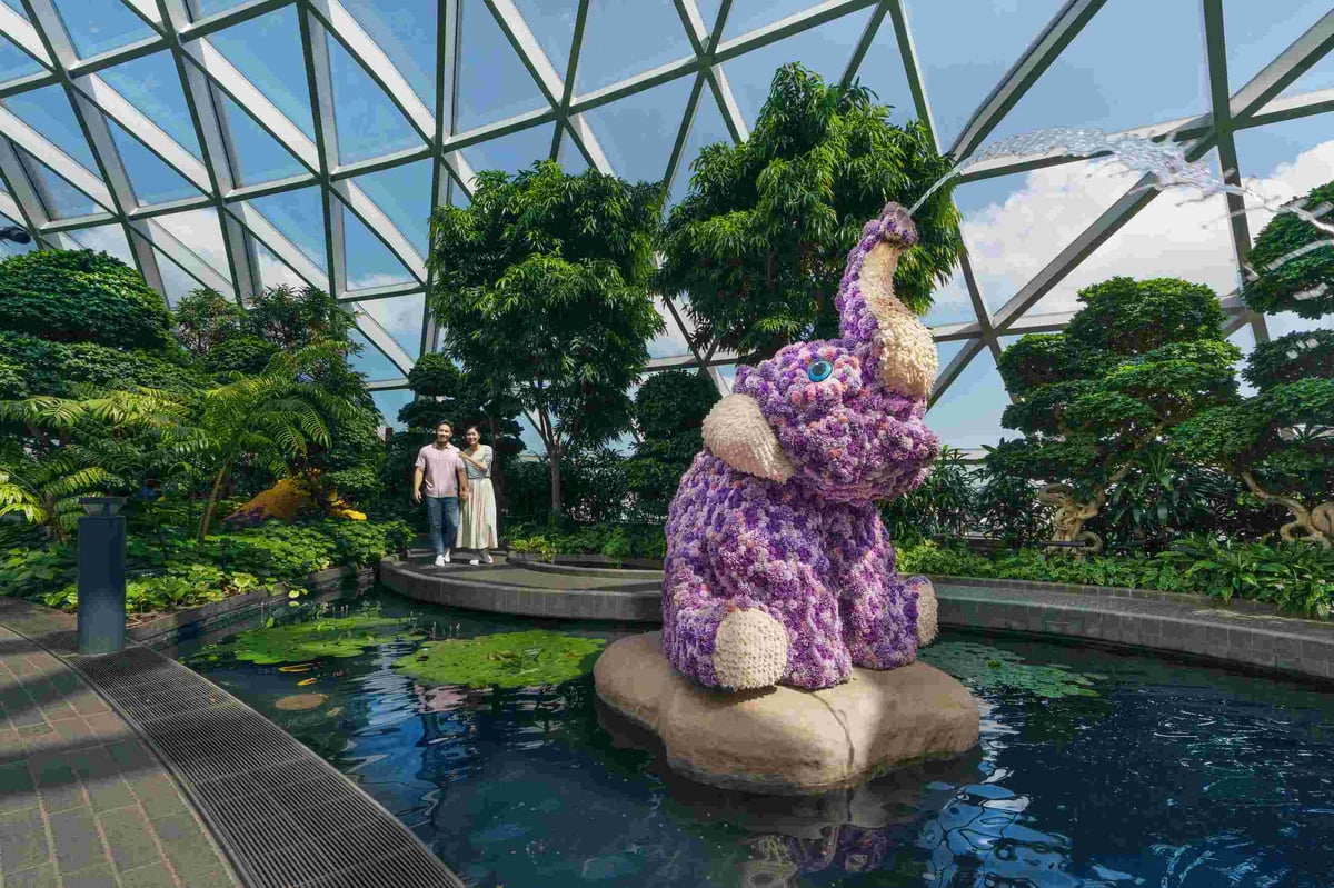 Flower elephant sculpture spraying water at Canopy Park, Jewel Changi Airport Singapore, surrounded by lush greenery under glass dome.