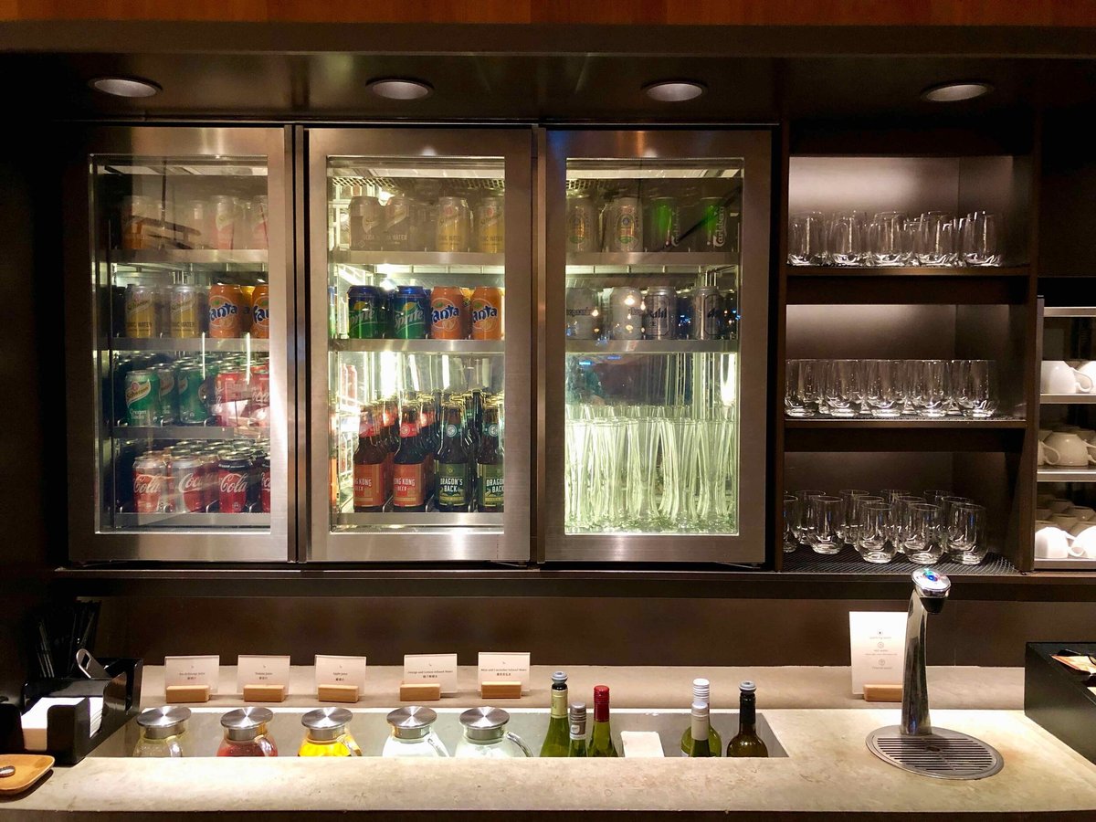 The beverage station at The Pier Business Class Cathay Pacific Lounge HKG, featuring a glass door fridge stocked with soft drinks, bottled beer and mineral water.