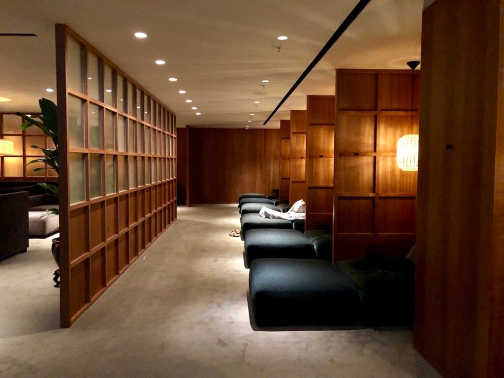 The Relaxation Room at The Pier Business Class Lounge in Hong Kong International Airport, featuring a row of plush daybeds separated by wooden partitions, dimmed lighting, and a tranquil atmosphere designed for napping or quiet rest.