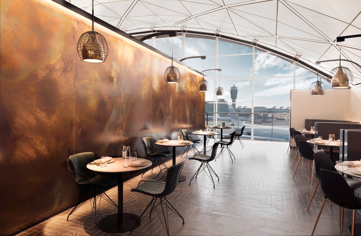 Stylish interior of the Centurion Lounge at Hong Kong International Airport featuring a sleek monochrome palette, designer seating, geometric ceiling, and a modern cocktail bar overlooking the runway.