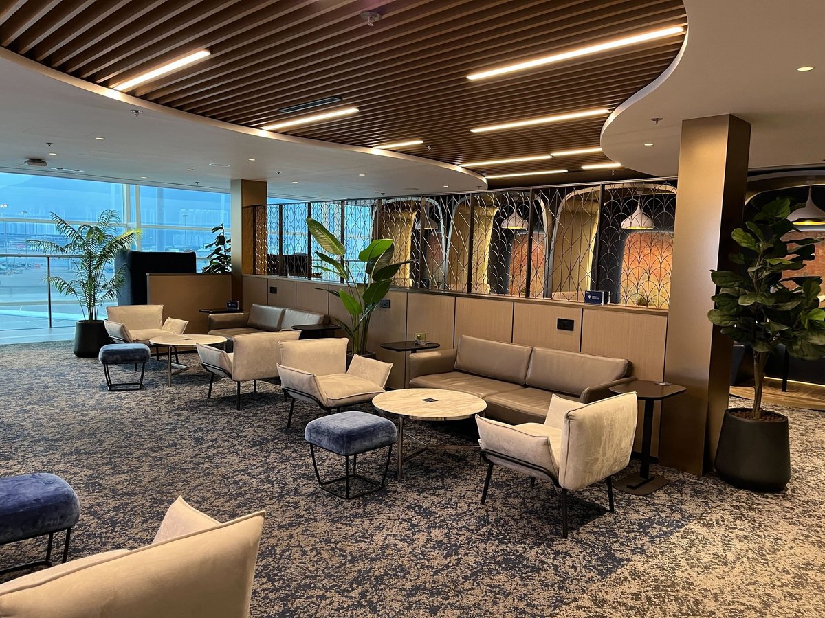 Modern seating area at Chase Sapphire Lounge Hong Kong Airport featuring plush armchairs, marble tables, and elegant wood-paneled ceilings overlooking the tarmac.