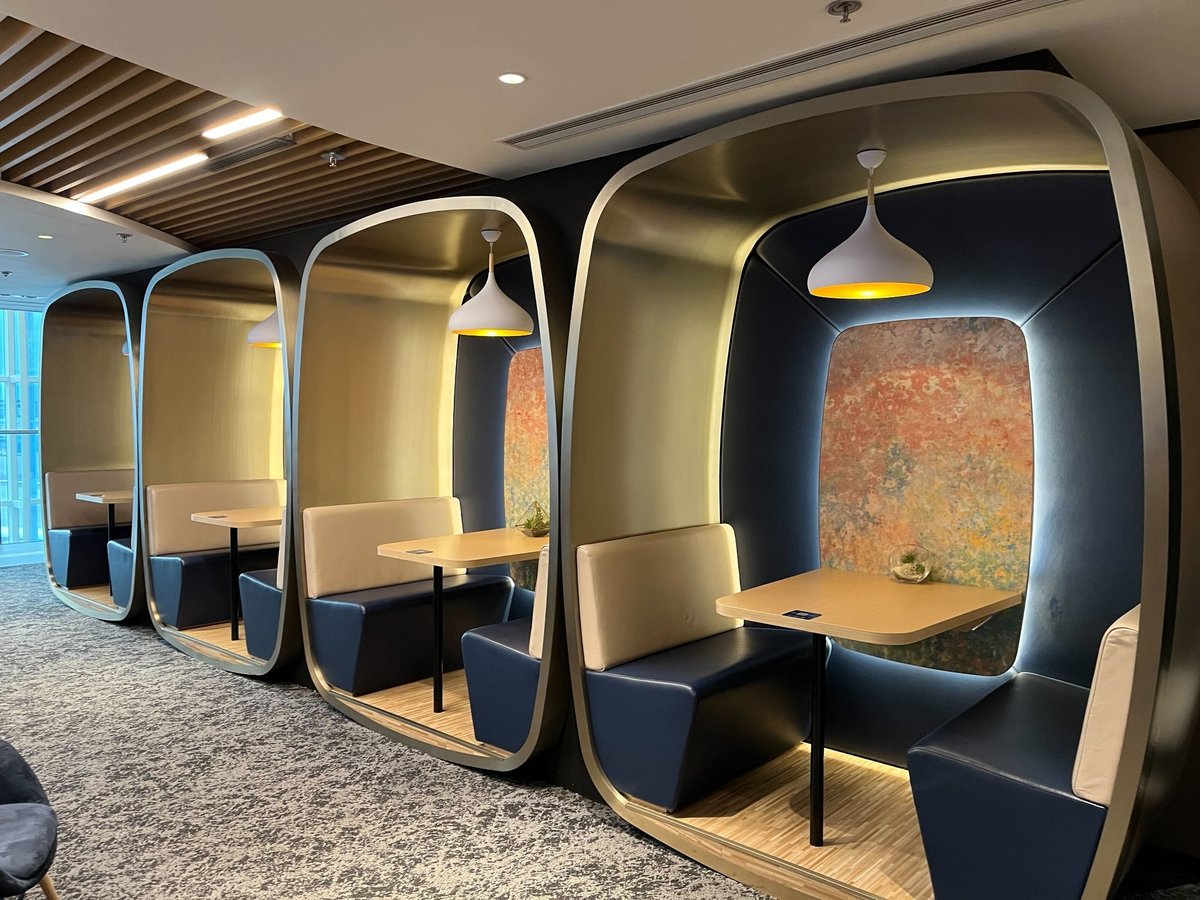 Modern semi-private dining booths with curved frames, pendant lighting, and abstract art backdrop at the Chase Sapphire Lounge Hong Kong Airport.