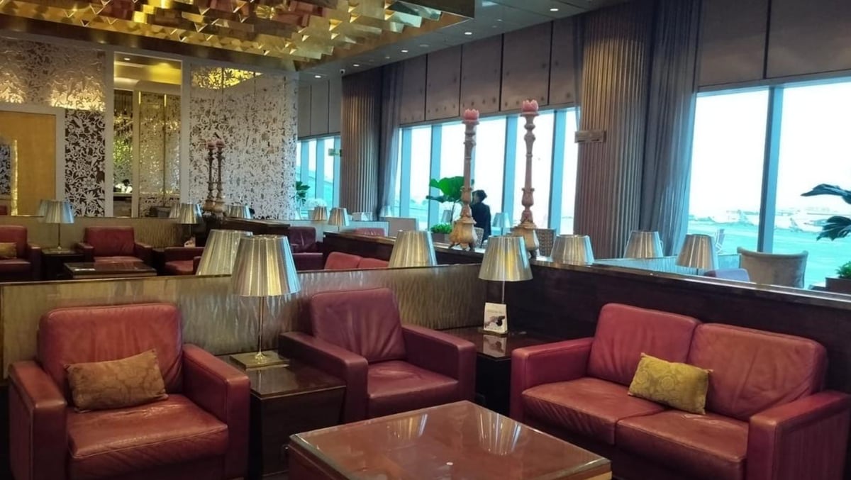 Ruby coloured leather seating options at the Adani Lounge Western Wing at Mumbai Airport, featuring wide windows that let in natural light and many lamps situated between the sofas.