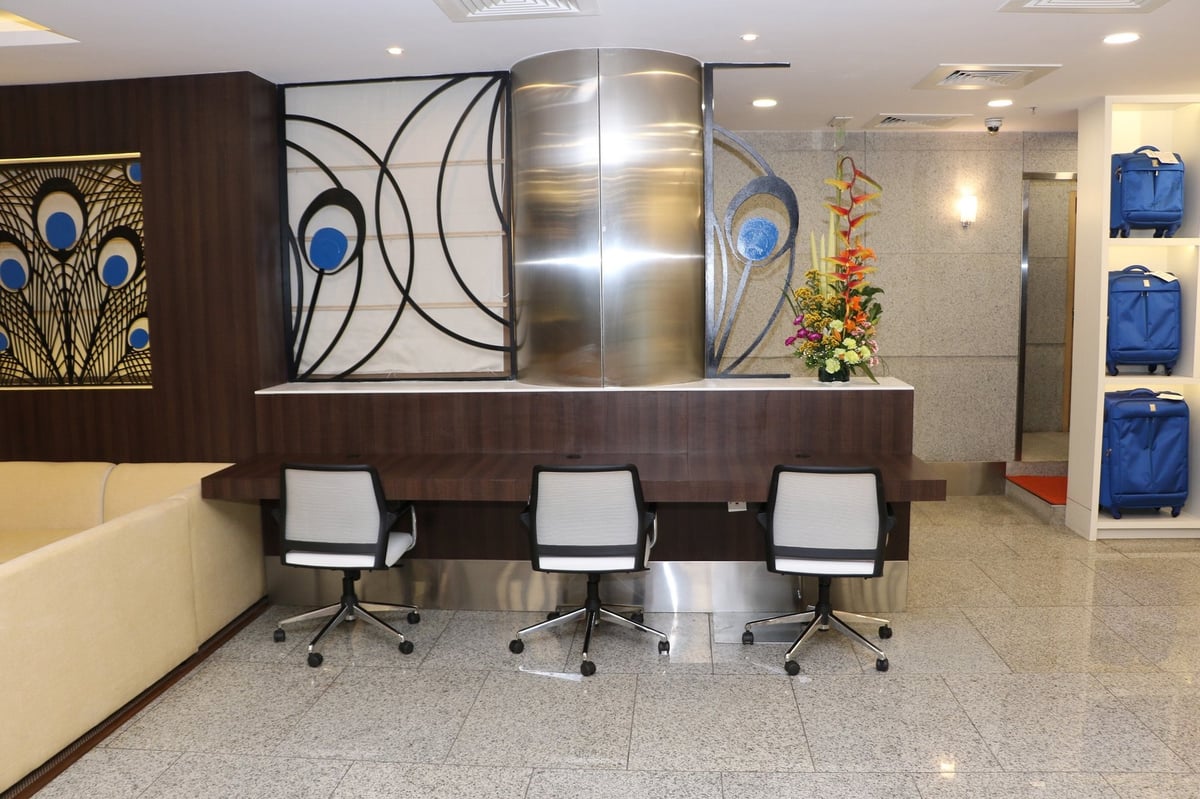 Desk workstation area at the West wing aviserv lounge at Mumbai Airport. There is a floral arrangement on the top of the counter/desk and three luggage depository areas in the wall to the right.