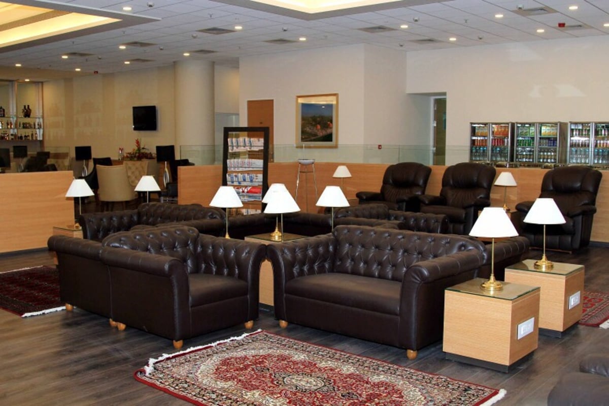Leather sofas and lamp fixtures at the Loyalty Lounge T2 Mumbai Airport. On the back wall there are beverage refrigerators.