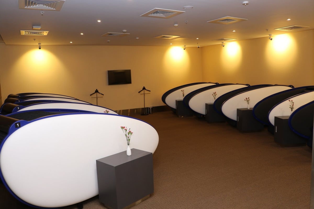 Sleeping pods at the aviserv lounge (western wing) t2 at Mumbai Airport. There are floral arrangements positioned next to the pods, and a tv in the middle of the back wall. The area is warmly lit.