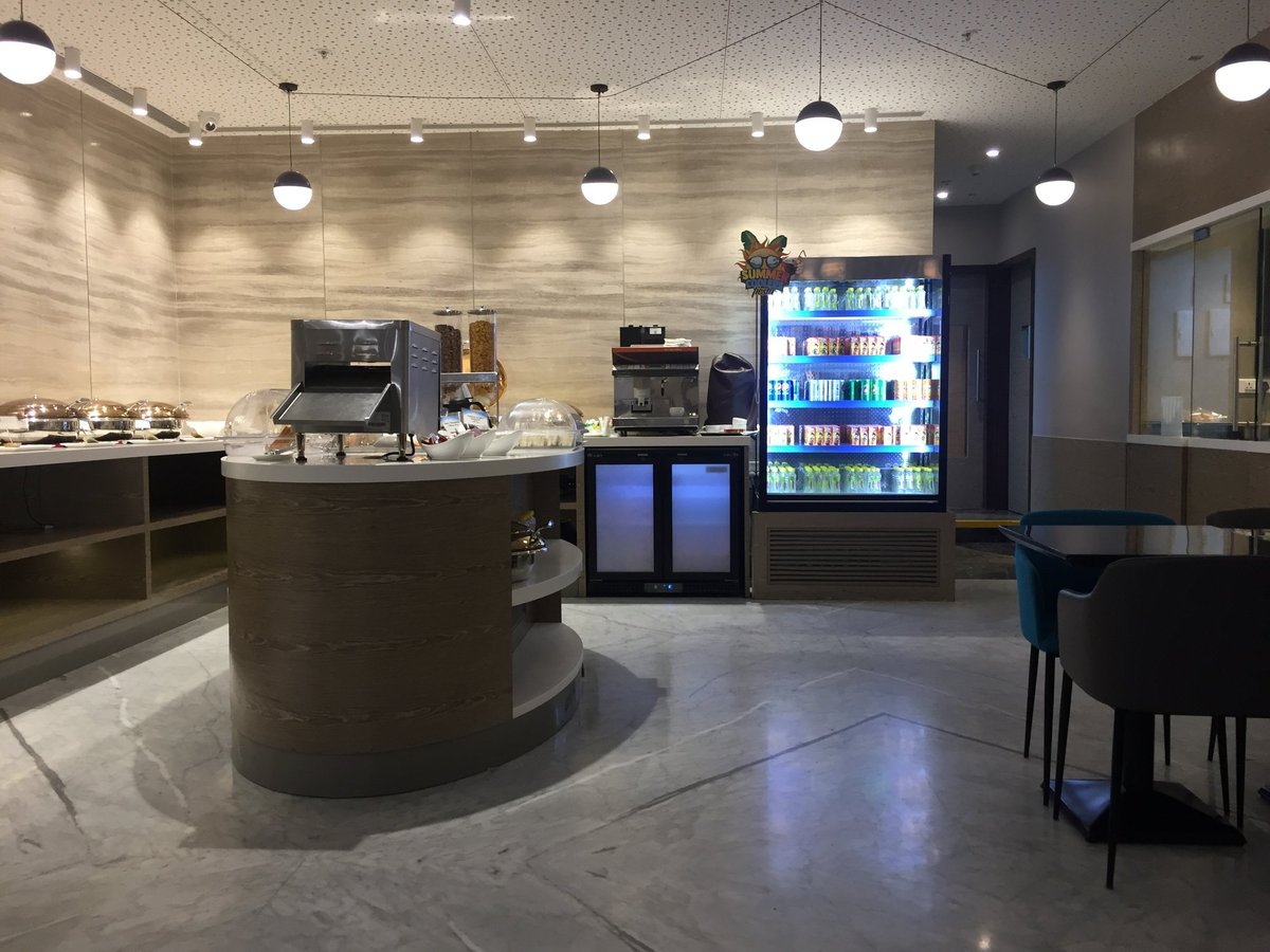 The buffet at the Travel Club lounge t1 Mumbai Airport featuring a beverage station, seating area and several hot dishes and snacks.