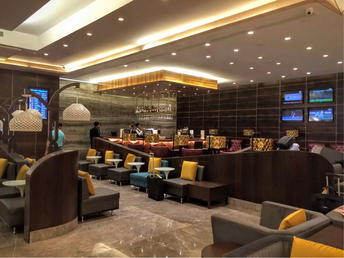 The Travel Club Lounge at Terminal 2 of Mumbai Airport, showcasing partitioned seating and variety of charcoal, blue, and ruby coloured armchairs with yellow pillows.