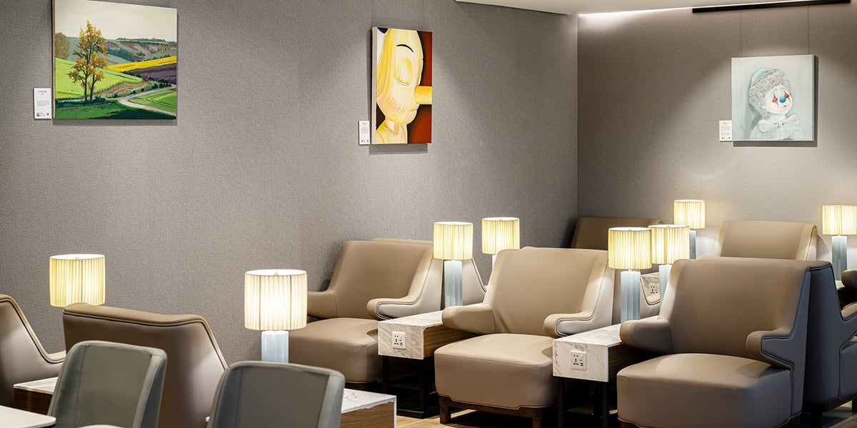 The plaza premium lounge at CKG airport Pier H, featuring a cozy seating area with beige armchairs, paired with small side tables, each equipped with individual power outlets. Soft warm lighting from the table lamps creates a warm ambiance.