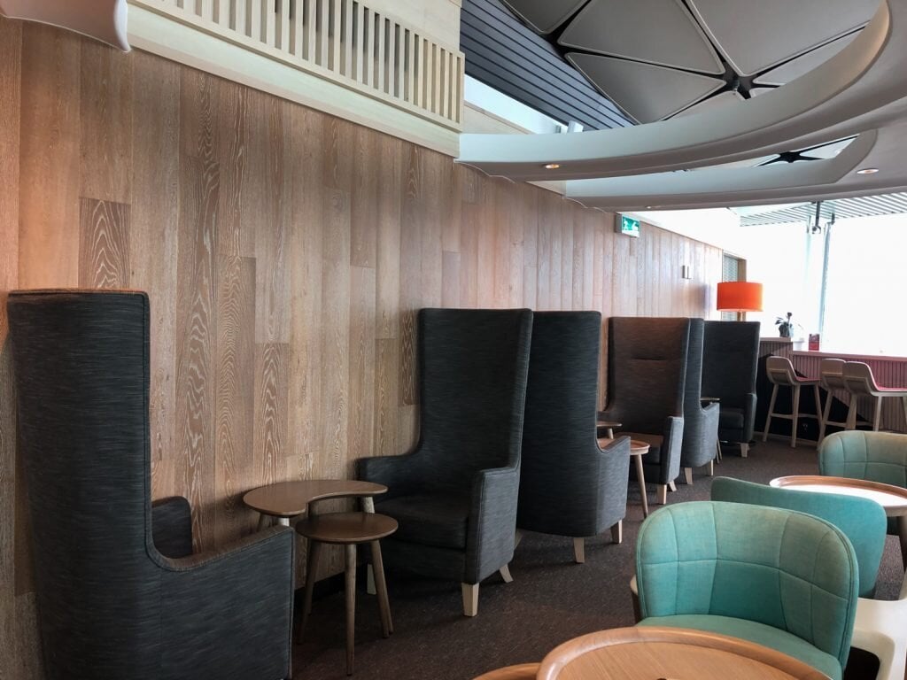 Quiet seating zone at Club Autus Lounge in Hong Kong International Airport, featuring tall privacy chairs with side tables against a wood-paneled wall, ideal for relaxation or focused work.