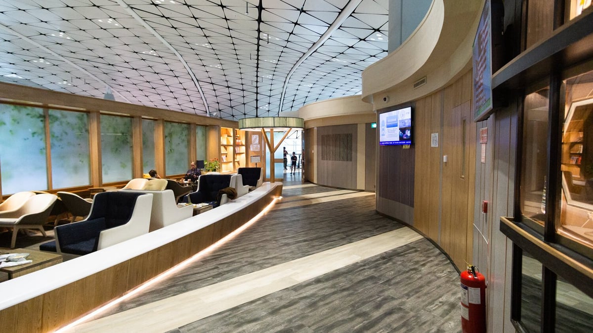 Interior of Club Autus Lounge at Hong Kong International Airport, featuring modern curved architecture, wood flooring, plush lounge seating, and a tranquil atmosphere near Gate 210 in the Midfield Concourse.