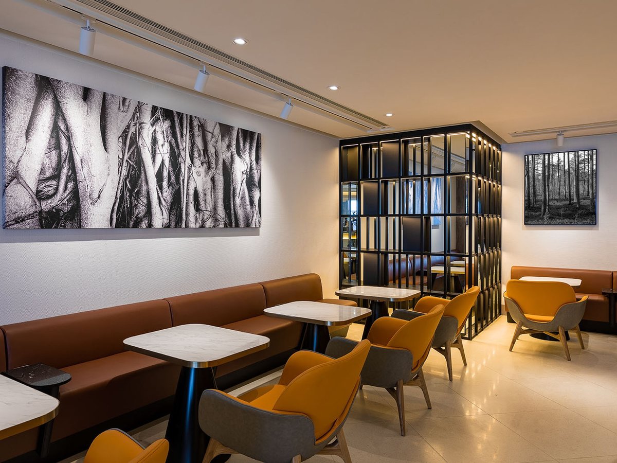 Elegant balcony seating area at Plaza Premium Lounge West Hall, Hong Kong International Airport, featuring panoramic terminal views, modern furnishings, and ambient lighting beneath a vaulted ceiling.