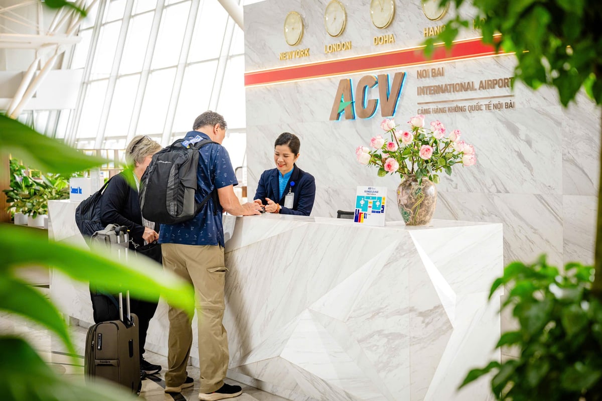 Reception area of the ACV Business Lounge at Hanoi Noi Bai International Airport. A staff member assists travelers at a modern white marble counter adorned with fresh flowers. World clocks displaying various time zones are mounted on the wall