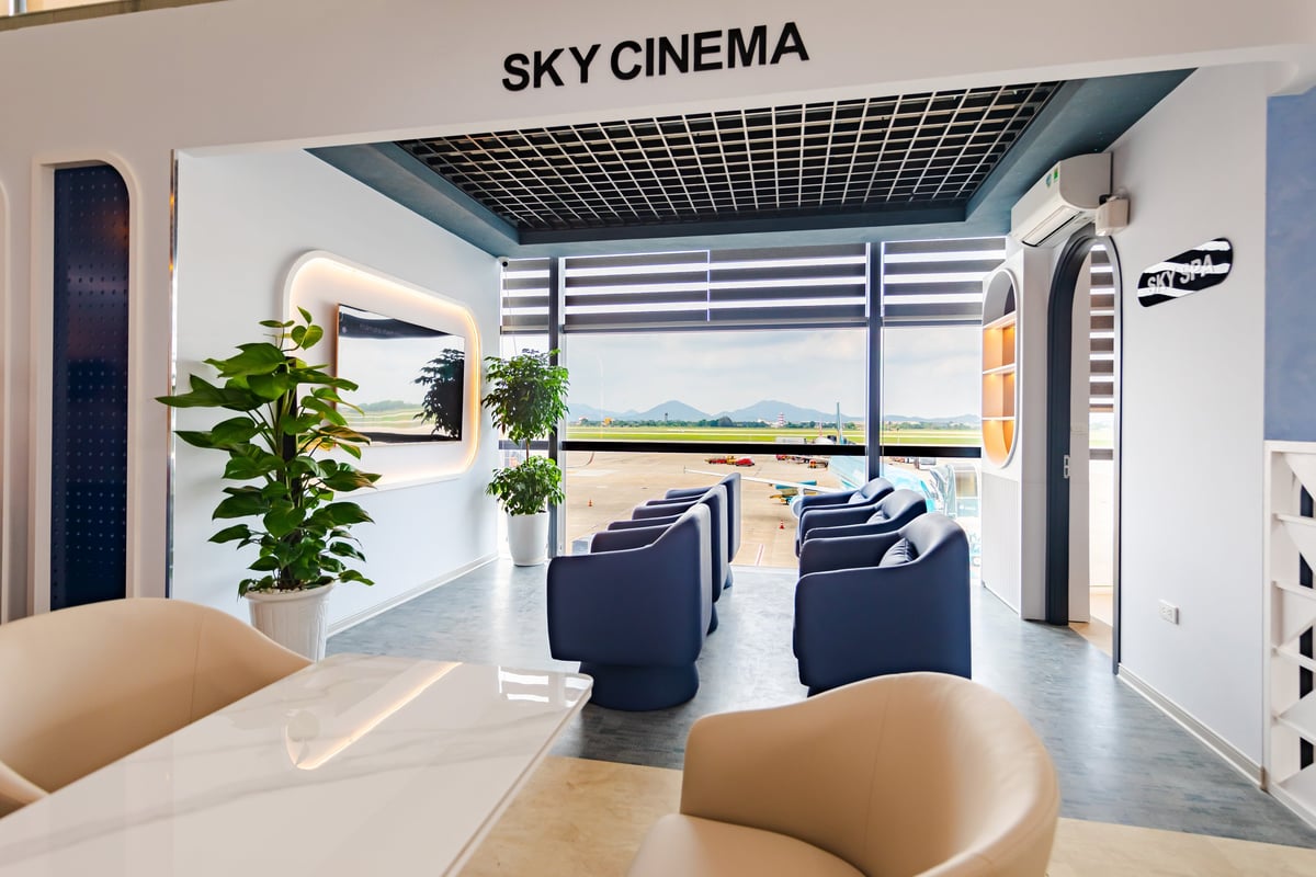 Sky Cinema area inside ASG Sky Lounge at Noi Bai Domestic Airport, featuring plush navy blue recliner chairs arranged in rows facing a large wall-mounted screen, and bright natural light from floor-to-ceiling windows overlooking the runway