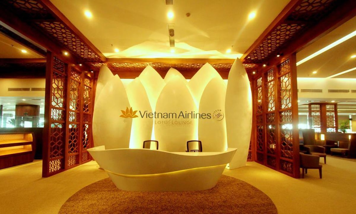 Vietnam Airlines Lotus Lounge reception area at Hanoi Airport. The reception desk has a modern, sculptural white design resembling the shape of a lotus flower. Behind it, large illuminated panels shaped like lotus petals create a striking backdrop.