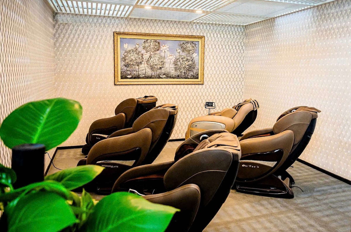 Massage chair relaxation room at ACV Business Lounge, Hanoi Airport, featuring a row of modern brown massage chairs arranged in a cozy, softly lit space with textured walls, framed artwork, and decorative indoor plants.