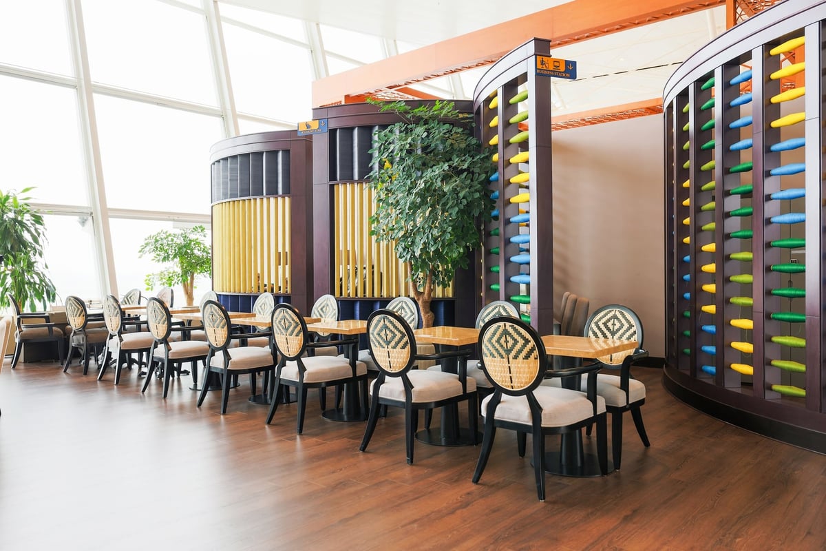 Dining area at the SH Premium Lounge, International Terminal, Hanoi Airport. The space features wooden floors, light wood tables, and cushioned chairs with patterned wicker backs.