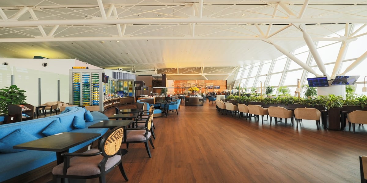 Spacious interior of the SH Premium Lounge at Hanoi International Airport, featuring large floor-to-ceiling windows that provide abundant natural light. The lounge has wooden flooring, a variety of seating arrangements including cushioned chairs