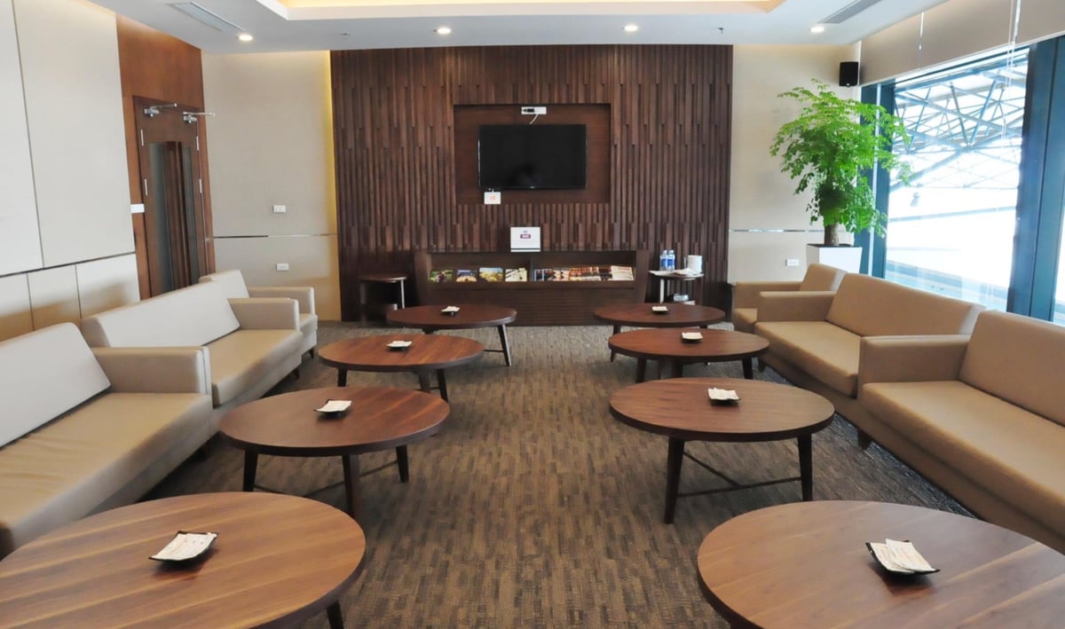 Vietnam Airlines Lotus Lounge seating area at Hanoi Airport. The space features beige upholstered sofas arranged along both walls, complemented by multiple round wooden coffee tables.