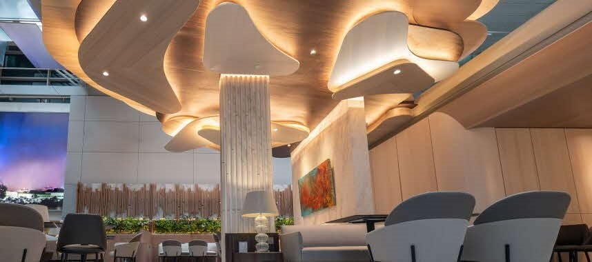Stylish interior of the DBS Private Bank Insignia Lounge at Changi Airport, featuring modern sculptural ceiling panels with soft backlighting, elegant light wood wall finishes, and comfortable grey seating