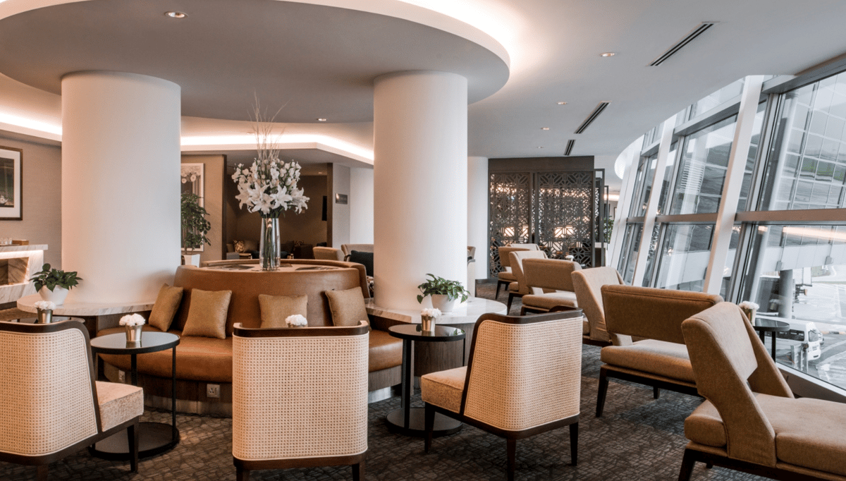 Seating area inside the Malaysia Airlines Domestic Golden Lounge at KLIA Terminal 1, featuring rattan-backed chairs, soft lighting, floral centerpieces, and large windows overlooking the terminal exterior.