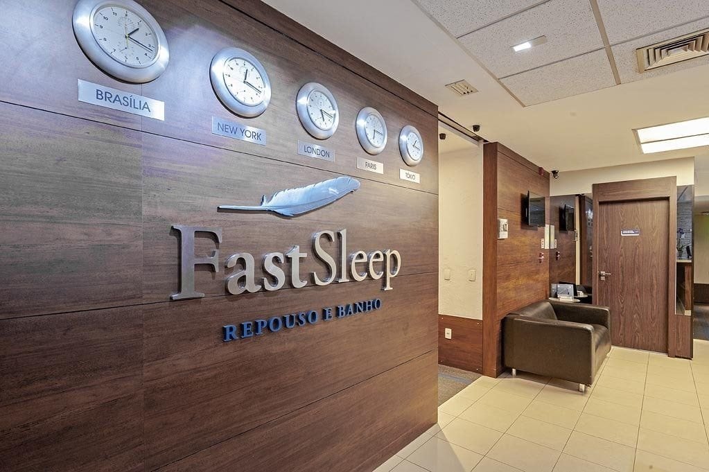 Fast Sleep Hotel at São Paulo Guarulhos Airport featuring world clocks, modern wood-panel design, and a cozy reception area for rest and showers