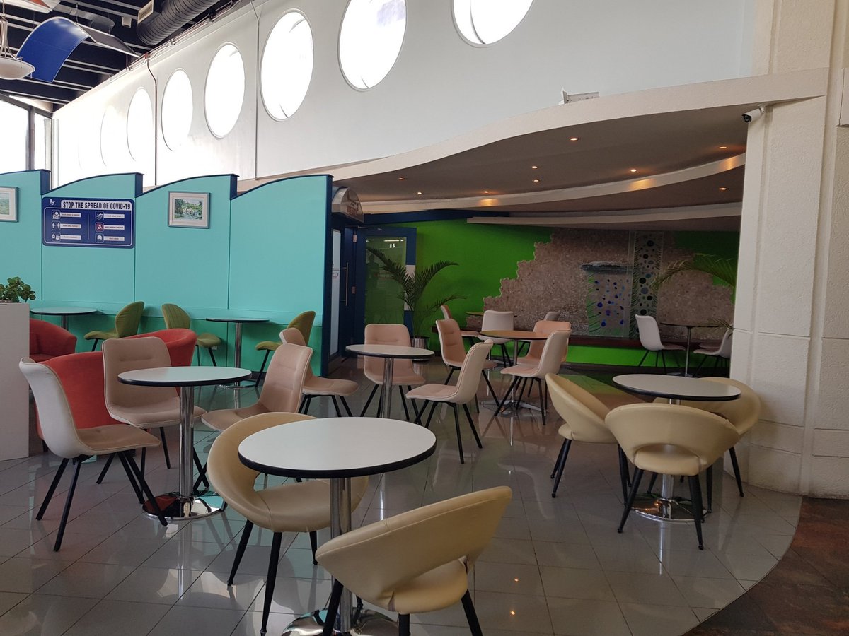 Casual dining area at the Airlines Executive Lounge in Grantley Adams International Airport, Barbados, featuring modern round tables, cushioned chairs, and a tropical-themed accent wall.