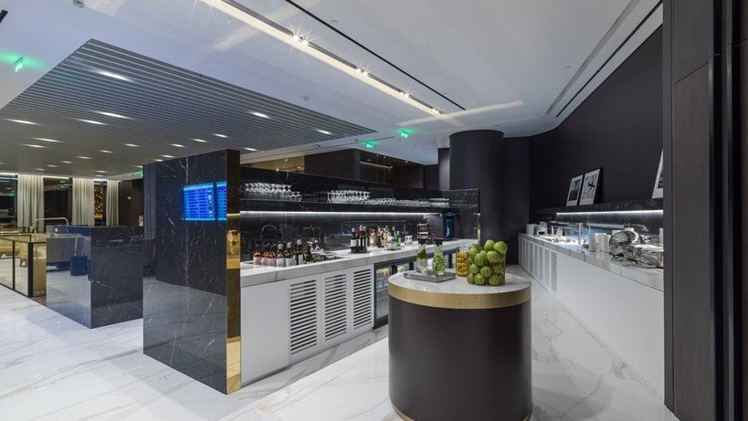 The Goldair Handling lounge at Hall A Athens Airport. It features a sleek bar design and dark marble countertops, with a white marble floor. The space includes a well stocked bar, with bottles and glassware on display.