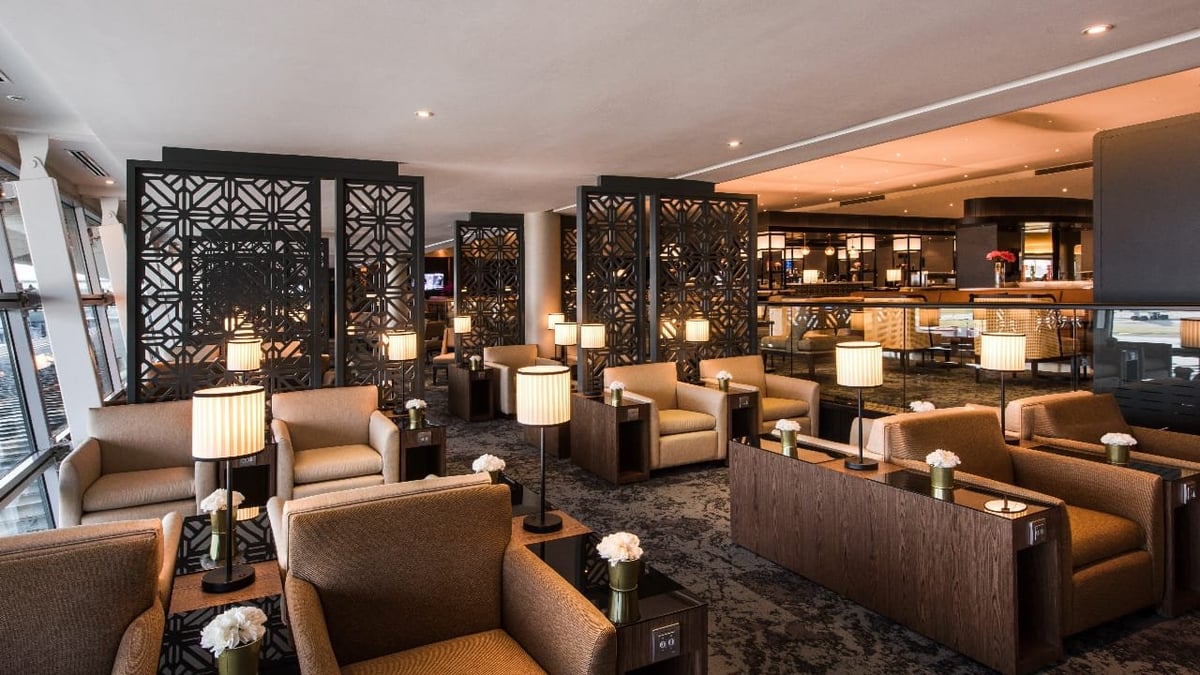 Elegant seating area inside Malaysia Airlines' International Golden Lounge at KLIA Satellite Terminal, featuring plush armchairs, privacy screens with intricate geometric patterns, ambient lighting, and a view of the dining area in the background.