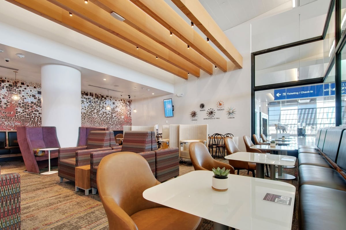 pacious seating area of the Escape Lounge in Terminal 3 at Phoenix Sky Harbor International Airport, featuring modern decor with comfortable chairs, dining tables, and natural light streaming through floor to ceiling glass walls.