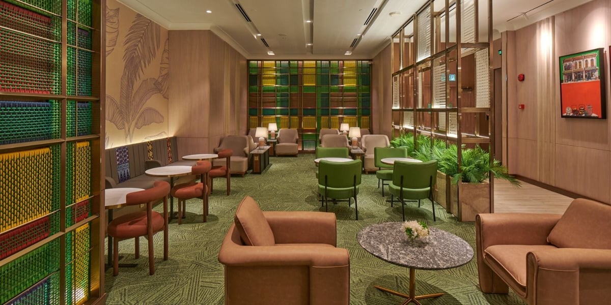 Sophisticated and warm seating area of the plaza premium lounge at Kuala Lumpur International Airport. The decor is largely wooden with various browns hues, complimented by foliage in the background and some green seating booths off to the side.