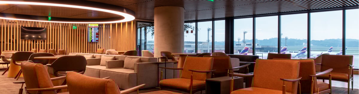 Modern seating area at Plaza Premium Lounge in São Paulo Guarulhos Airport’s domestic terminal, featuring warm-toned armchairs, sleek lighting, wood panel accents, panoramic apron views, and LATAM aircraft visible through floor-to-ceiling windows.