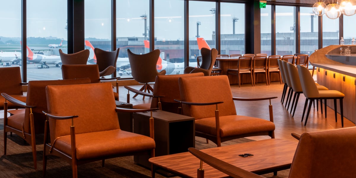 Spacious relaxation area at Plaza Premium Lounge in São Paulo GRU Airport’s domestic terminal, featuring mid-century modern leather armchairs, stylish bar seating, and floor-to-ceiling windows with views of GOL aircraft parked at the gate.
