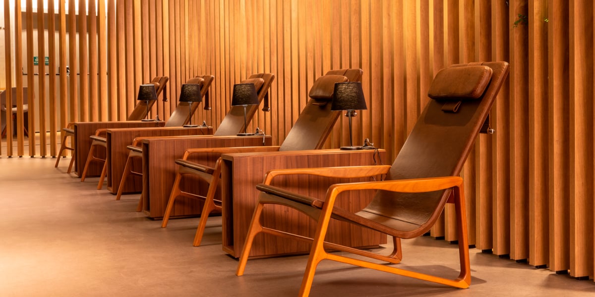Row of elegant leather recliners with individual side tables and reading lamps in the relaxation area of Plaza Premium Lounge at São Paulo GRU Airport’s domestic terminal, surrounded by warm wooden paneling for a serene travel experience.