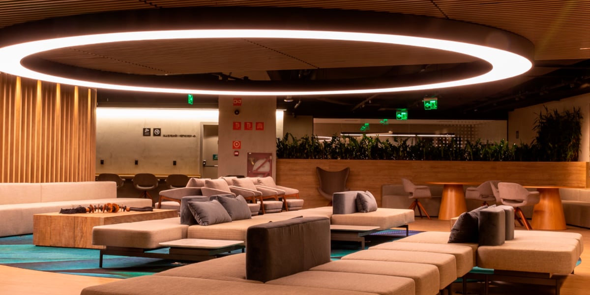 Plaza Premium Lounge at Terminal 2 Domestic Airside, featuring a sleek contemporary design with neutral-toned modular sofas, plush cushions, wood-accented walls, a dramatic circular LED ceiling light, and ample seating for travelers