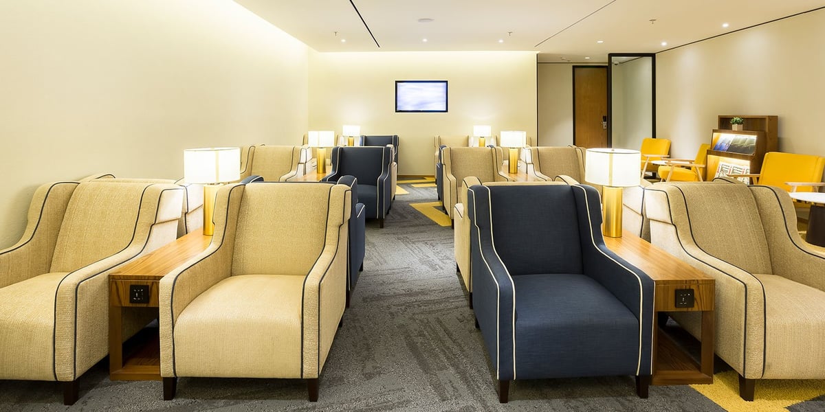 Quiet seating lounge in the arrivals Plaza Premium Lounge at GIG Airport, featuring rows of beige and navy armchairs with integrated power outlets, soft lighting, and a relaxed atmosphere designed for post-flight comfort.