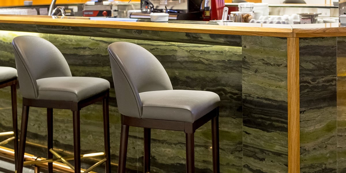 Close-up of sleek leather bar stools at the domestic Plaza Premium Lounge in Rio de Janeiro GIG Airport, set against a polished green stone counter with wood trim and soft underlighting, creating a refined and modern bar atmosphere.