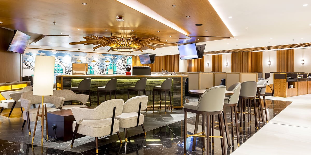 Contemporary dining area in the domestic Plaza Premium Lounge at GIG Airport, featuring a sleek central bar with high stools, cozy seating arrangements, artistic ceiling lighting, and a colorful wall mural adding a vibrant touch.
