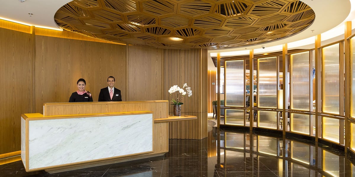 Elegant reception area of Plaza Premium Lounge at Rio de Janeiro GIG International Airport, featuring uniformed staff behind a marble and wood desk, modern geometric ceiling design, and warm ambient lighting in Terminal 2.